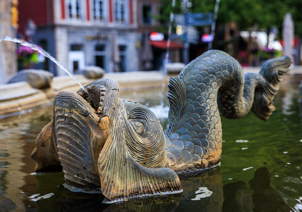 Detailaufnahme einer Drachenfigur am Karlsbrunnen in Aachen, aus deren Maul Wasser sprudelt.