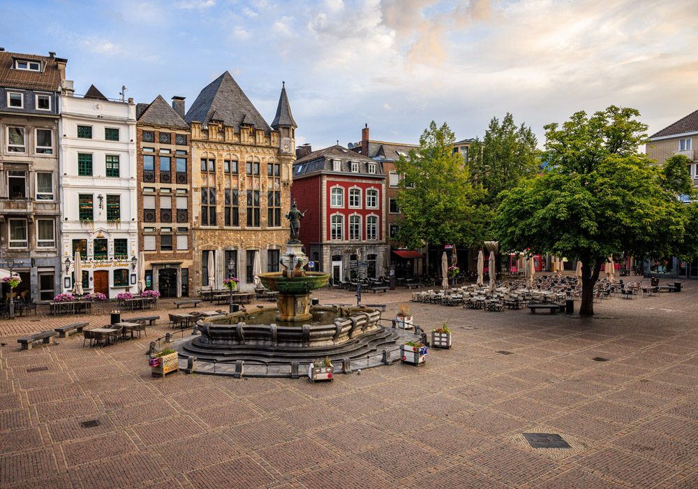 Der Aachener Marktplatz mit dem Karlsbrunnen im Vordergrund und historischen Zunfthäusern im Abendlicht.