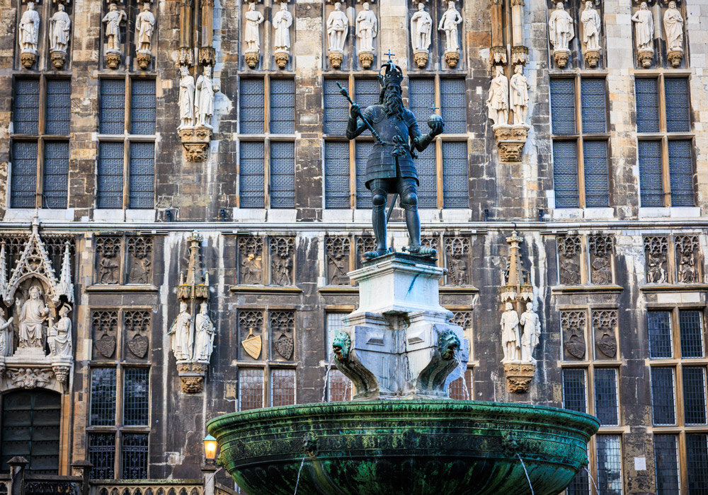 Die Statue Karls des Großen auf dem Karlsbrunnen vor der gotischen Fassade des Aachener Rathauses.