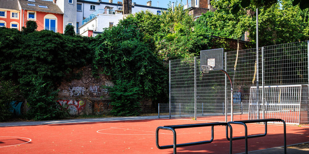 Basketballplatz im Soermondtpark in Aachen mit Ballfangzaun, umgeben von Wohnhäusern und Grünflächen.