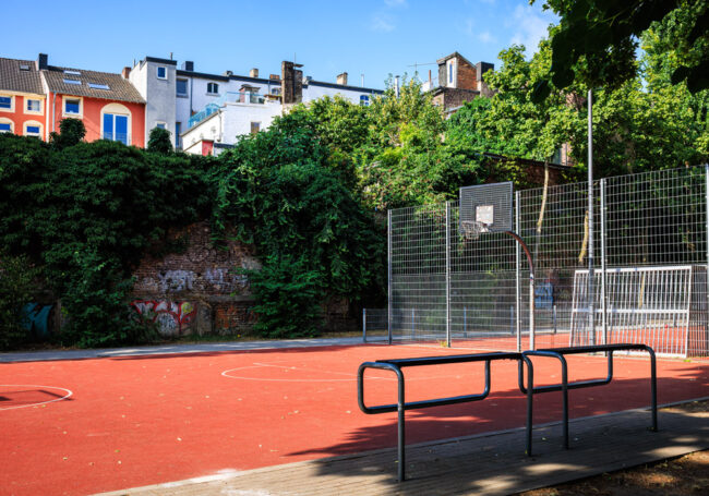 Basketballplatz im Soermondtpark in Aachen mit Ballfangzaun, umgeben von Wohnhäusern und Grünflächen.