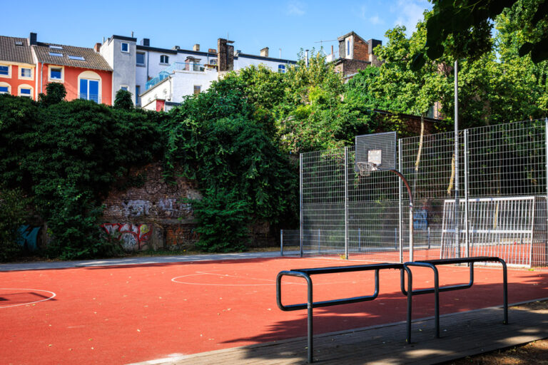 Basketballplatz im Soermondtpark in Aachen mit Ballfangzaun, umgeben von Wohnhäusern und Grünflächen.