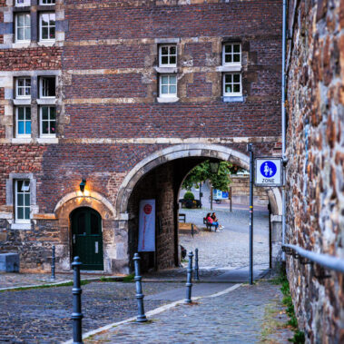 Rückseite des Burtscheider Abteitors mit Backsteinfassade, Torbogen und Kopfsteinpflaster, im Hintergrund eine Sitzgruppe im Innenhof