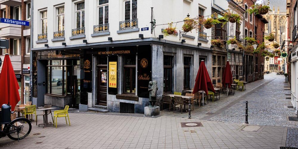 Eckhaus des Café Van den Daele in der Aachener Altstadt mit roten Sonnenschirmen und gelben Stühlen vor der Fassade
