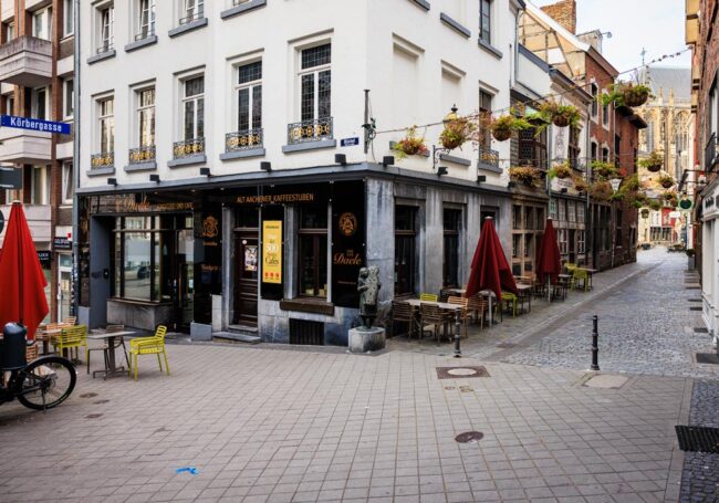 Eckhaus des Café Van den Daele in der Aachener Altstadt mit roten Sonnenschirmen und gelben Stühlen vor der Fassade