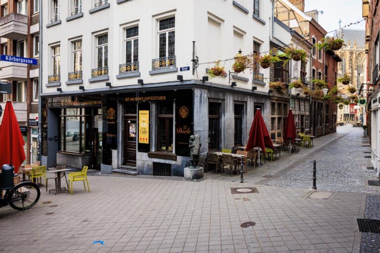 Eckhaus des Café Van den Daele in der Aachener Altstadt mit roten Sonnenschirmen und gelben Stühlen vor der Fassade