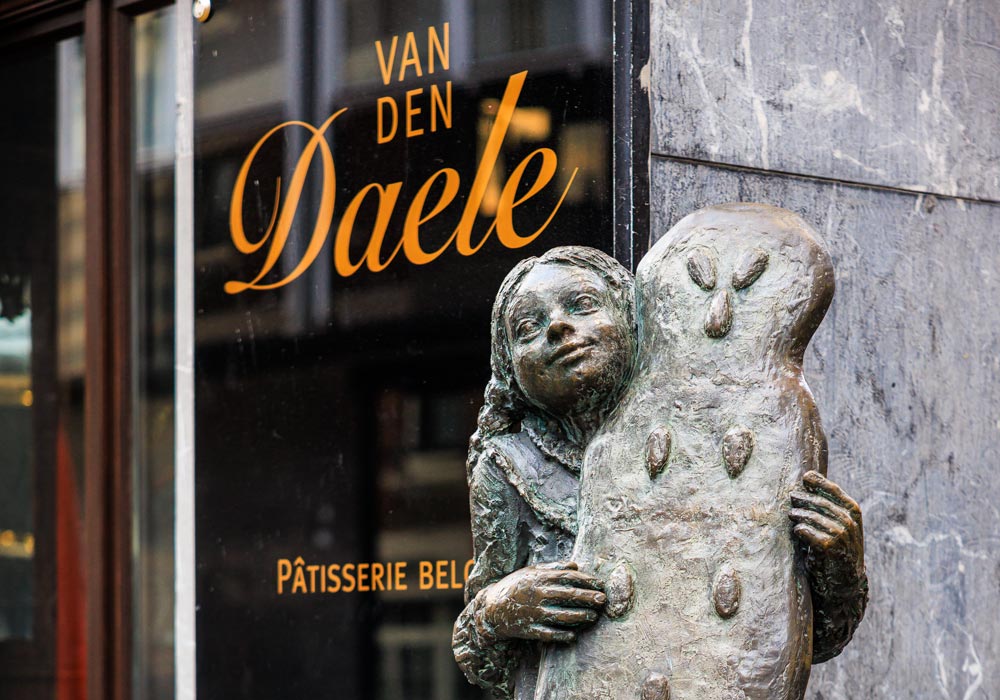 Bronzefigur eines Mädchens mit einem Reisfladen vor dem Schaufenster des Café Van den Daele