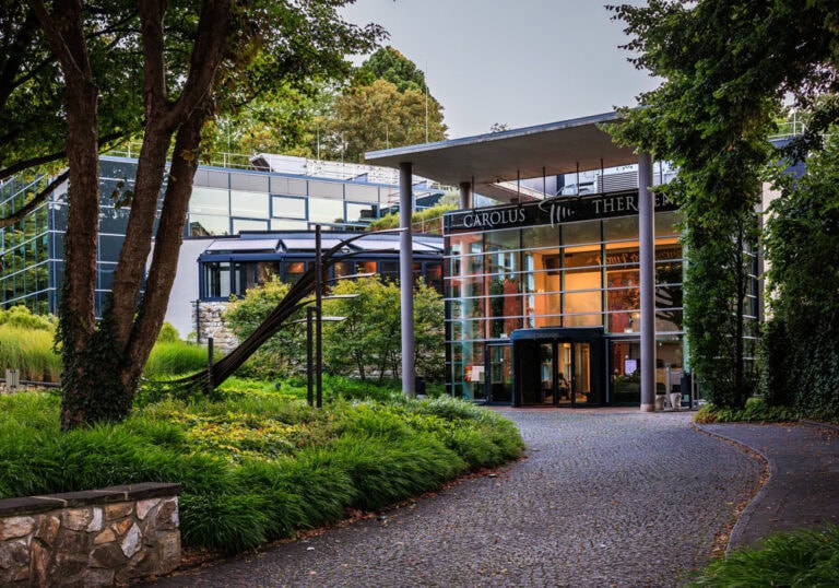 Carolus Thermen Aachen – Eingangsbereich Gläserner Eingangsbereich der Carolus Thermen Aachen mit Schriftzug, umgeben von Grünanlagen