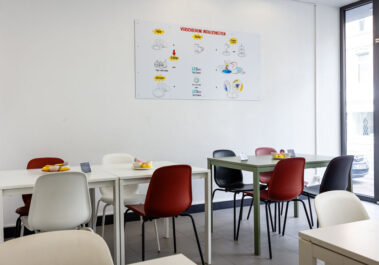 Heller Sitzbereich mit Tischen und bunten Stühlen im Keramik-Malstudio Farbenfleck Aachen, an der Wand ein Poster mit den verschiedenen Bemal-Möglichkeiten
