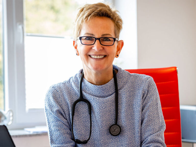 Porträt von Angelika Sailer, Hausärztin in Aachen-Soers, mit Stethoskop in ihrer Praxis