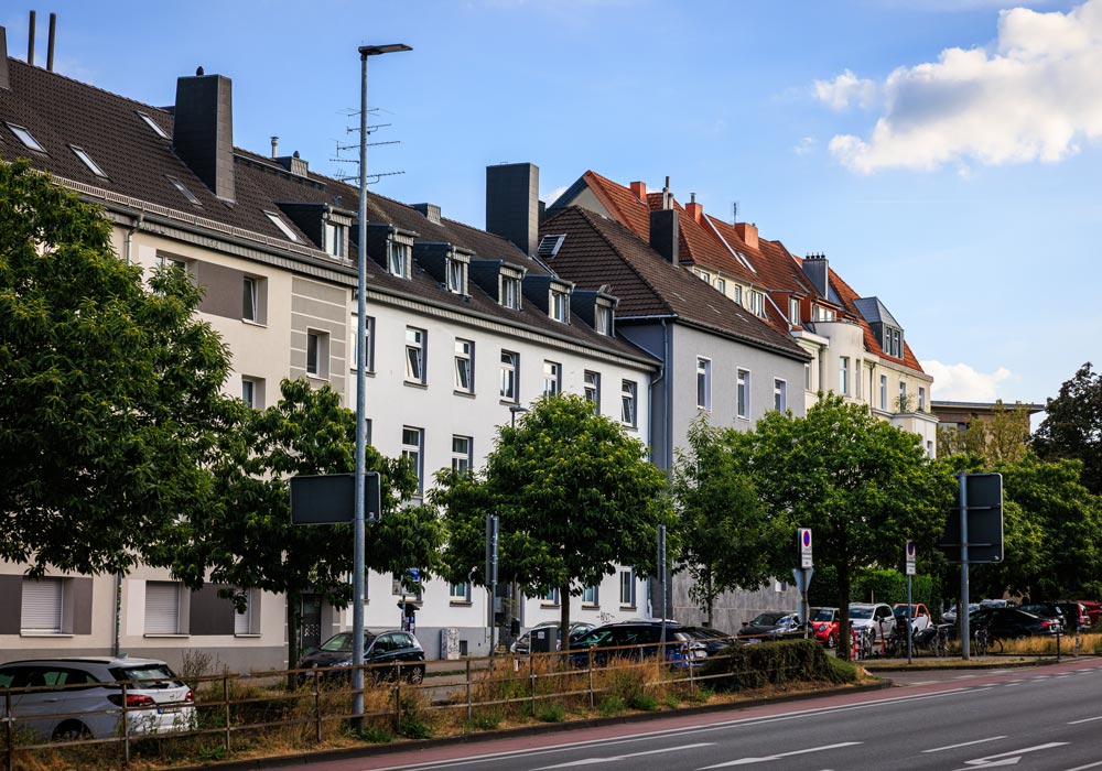 Wohnhäuserzeile am Pontwall in Aachen mit unterschiedlichen Fassaden und Dachformen, gesäumt von Bäumen und parkenden Autos
