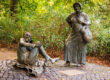 Bronzestatuen von Bauersfrau und Teufel am Denkmalplatz auf dem Lousberg, umgeben von herbstlichem Grün