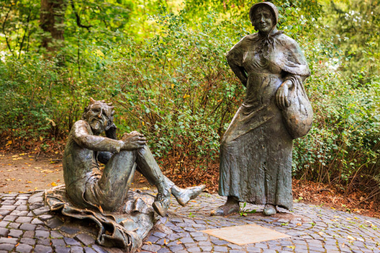 Bronzestatuen von Bauersfrau und Teufel am Denkmalplatz auf dem Lousberg, umgeben von herbstlichem Grün
