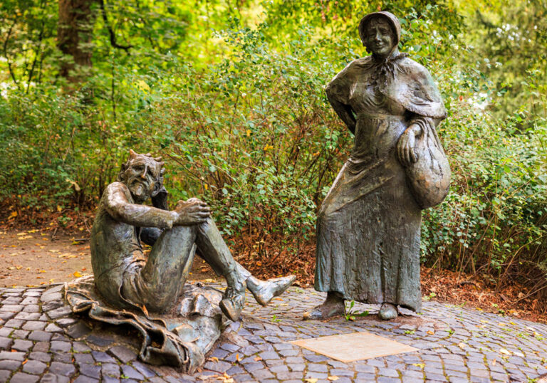 Bronzestatuen von Bauersfrau und Teufel am Denkmalplatz auf dem Lousberg, umgeben von herbstlichem Grün