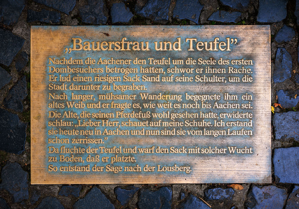 Bronzetafel mit dem Text der Lousbergsage „Bauersfrau und Teufel" auf dem gepflasterten Denkmalplatz am Lousberg