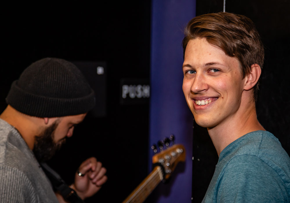 Lukas Flott lächelt in die Kamera, im Hintergrund ein Bandmitglied mit E-Bass