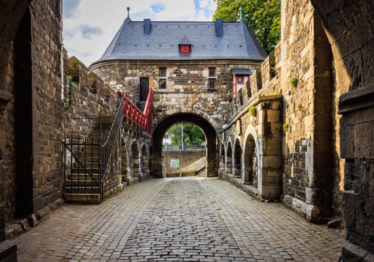 Kopfsteingepflasterter Torhof des Aachener Ponttors mit Blick auf den Hauptturm, rechts eine rote Freitreppe mit schmiedeeisernem Geländer