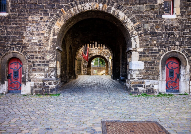 Zwei rote Türen mit dunklem schmiedeeisernem Zierbeschlag unter dem Torbogen des Aachener Ponttors