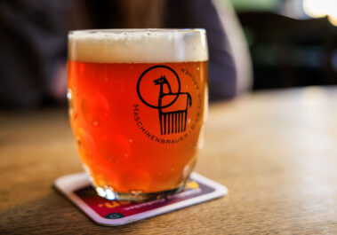 Bierglas mit dem Logo der Aachener Maschinenbrauer im Postwagen Zum Ratskeller, im Hintergrund unscharf ein Gast
