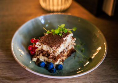 Tiramisu im Postwagen Zum Ratskeller mit Kakaopulver, roten Johannisbeeren, Blaubeeren und frischer Minze in einer blaugrünen Schale