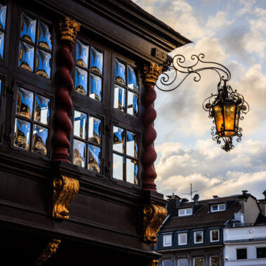 Fassadendetail des Postwagens am Aachener Markt mit goldenen Schnitzereien, gedrehten Holzsäulen und schmiedeeiserner Laterne im Abendlicht