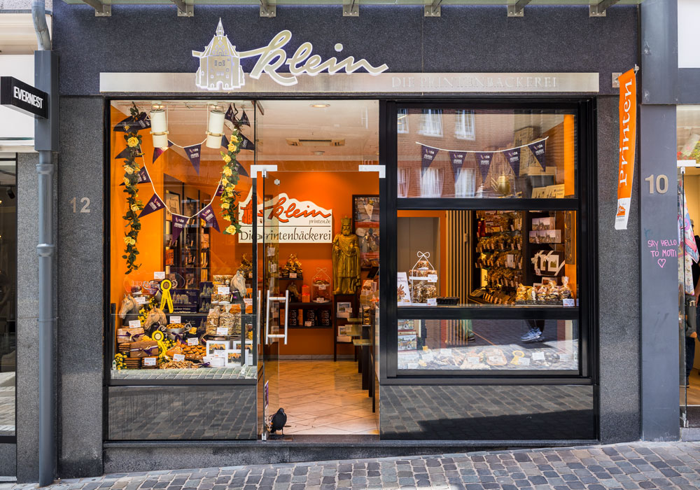 Ladenfront von Printen Klein in der Krämerstraße in Aachen mit beleuchtetem Schaufenster, Printen-Auslage und Fähnchen-Dekoration