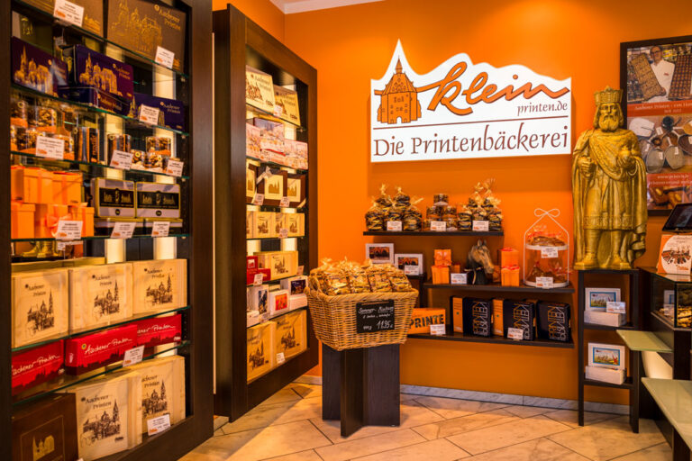 Innenraum von Printen Klein in der Krämerstraße mit Regalen voller Printenpackungen, goldener Karlsstatue und dem Schriftzug „Die Printenbäckerei"
