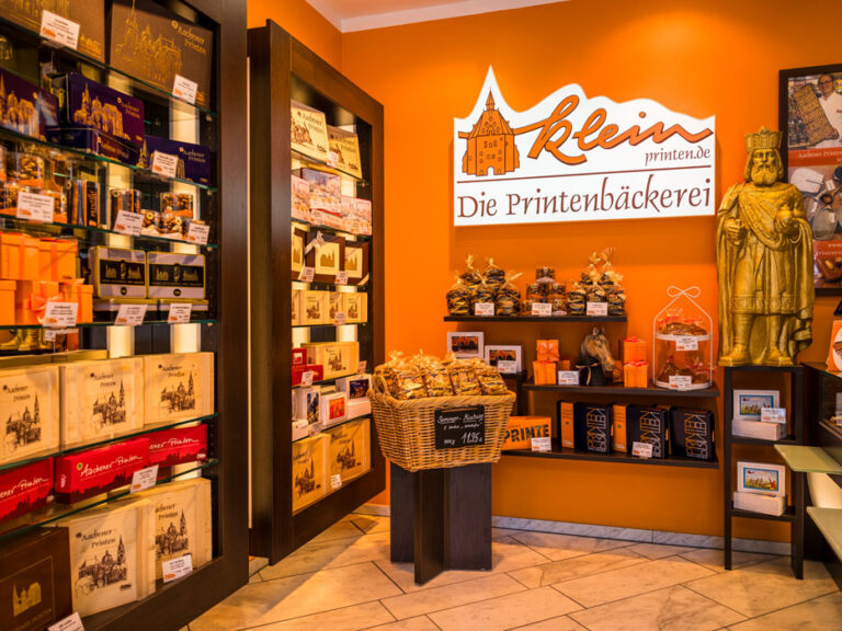 Innenraum von Printen Klein in der Krämerstraße mit Regalen voller Printenpackungen, goldener Karlsstatue und dem Schriftzug „Die Printenbäckerei"