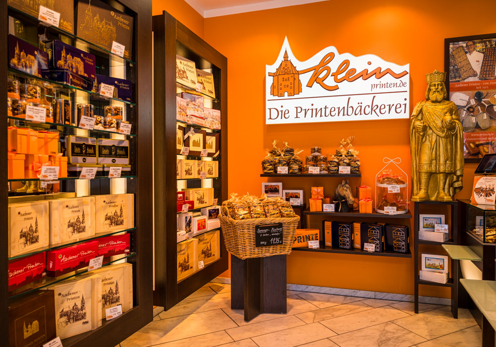 Innenraum von Printen Klein in der Krämerstraße mit Regalen voller Printenpackungen, goldener Karlsstatue und dem Schriftzug „Die Printenbäckerei"