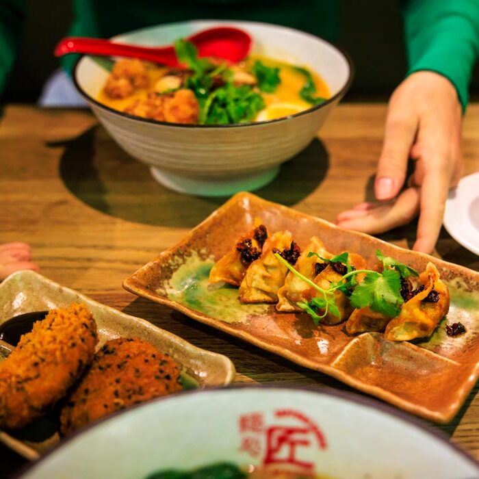 Tischszene bei Takumi Aachen mit Süßkartoffel-Kroketten, Gyoza und einer Ramen-Schüssel im Hintergrund, dazu eine Tasse grüner Tee