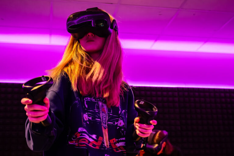 Blauwal VR-Café Aachen – Spielerin mit Controllern Spielerin mit VR-Brille und Controllern in magentafarbenem Licht im Blauwal VR-Café Aachen