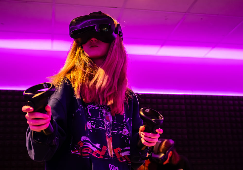Spielerin mit VR-Brille und Controllern in magentafarbenem Licht im Blauwal VR-Café Aachen