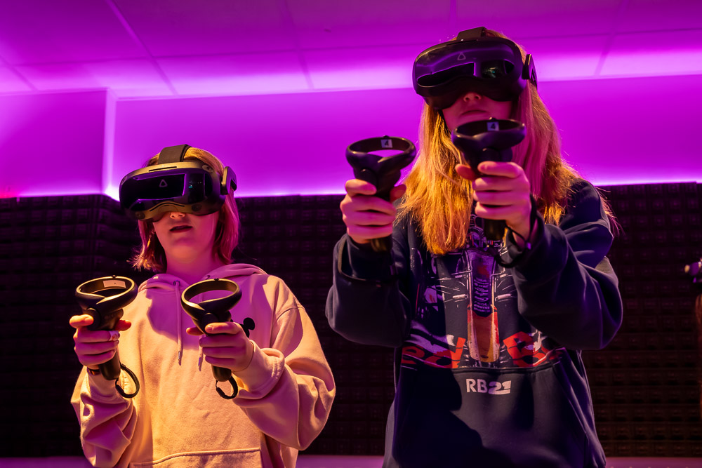 Zwei Mädchen mit VR-Headsets und Controllern in pink-violettem Licht im Blauwal VR-Café Aachen