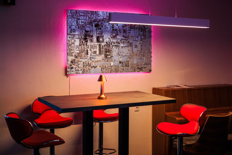 Stehtisch mit roten Barhockern und beleuchteter Wandkunst aus Elektronikteilen im Blauwal VR-Café Aachen