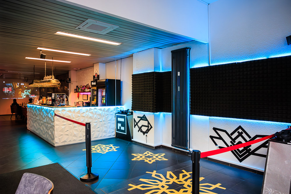Theke und Lounge im Blauwal VR-Café Aachen mit weißer Facettenfront, blauem Licht und gelben Bodenmustern